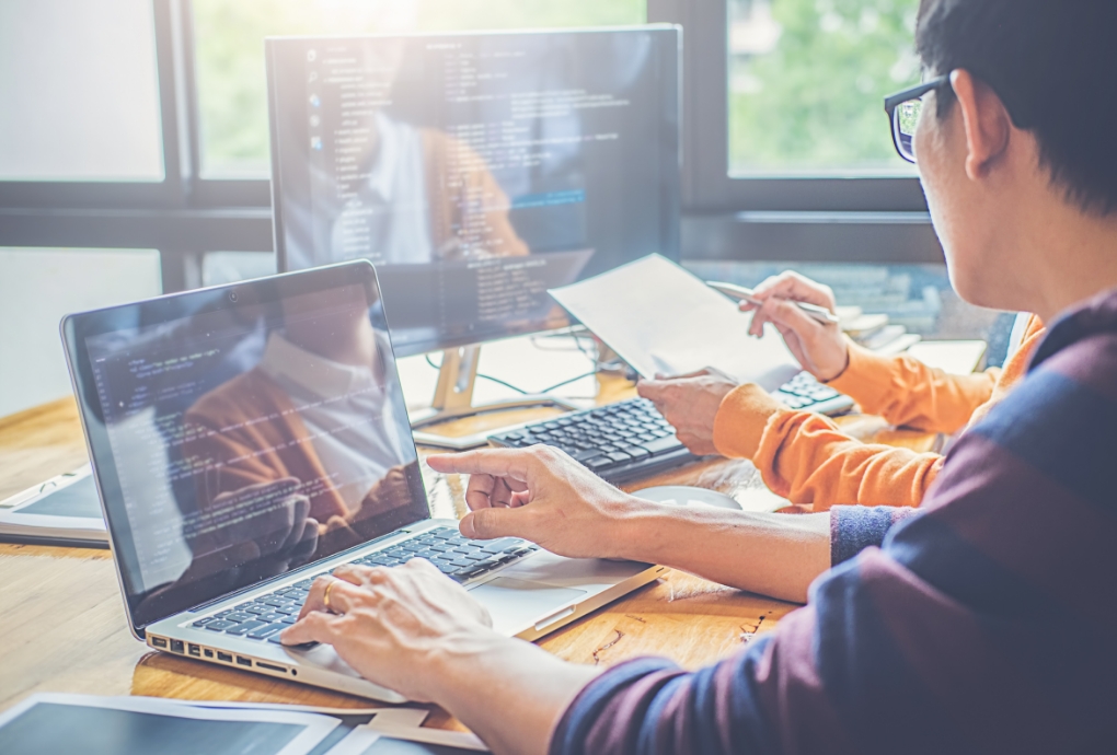 エンジニアがコードを確認しながら議論する様子。株式会社atombaseの受託開発事業でのチーム体制と高品質なシステム構築を象徴。