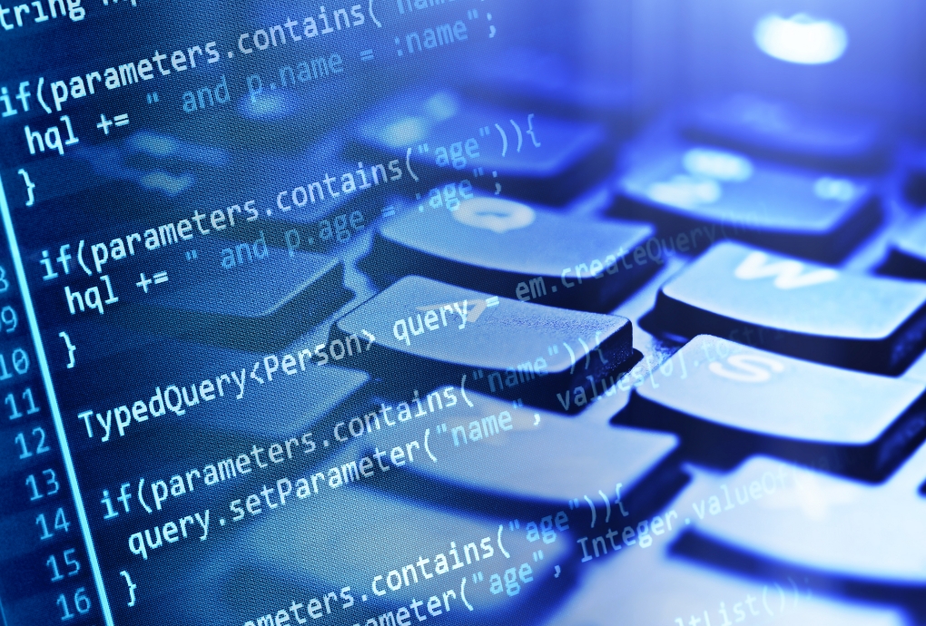 キーボード越しに映るソースコード。株式会社atombaseのシステムインテグレーション（SES）事業におけるエンジニア派遣・開発支援を表す。